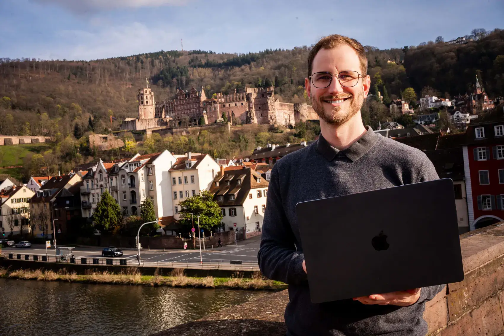 Joshua Stark mit MacBook vor dem Heidelberger Schloss und dem Neckar